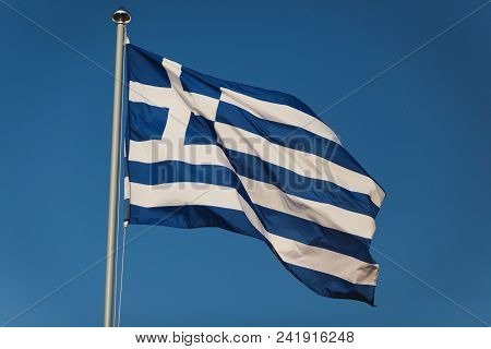 Greek Flag With Blue And White Colours Against Sky Background. Greek Banner Floats In Pure Cloudy Sk