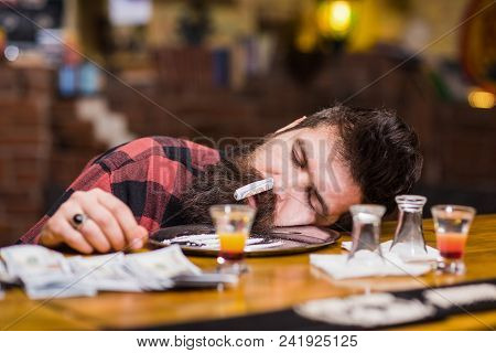 Guy Sleep With Rolled Banknote In Nostril, Defocused Background. Man With Sleeping Face Alone At Bar