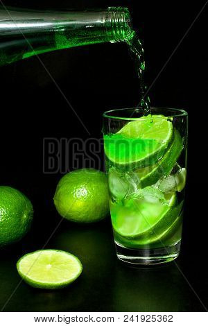 Glass Of Cold Green Lemonade With Ice And Fresh Ripe Green Limes On Black Background. Homemade Lemon