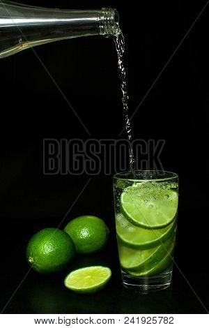 Summer Refreshing And Beverages Concept. Stream Of Cold Water From A Bottle Is Poured Into A Glass W