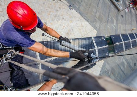 Industrial Climber, Alpinist, Is Passes Over Roof Edge. He Is Climb Down To Applying Silicone To Rub
