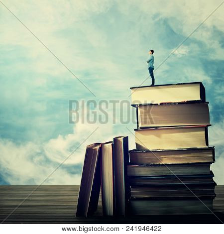 Young Student Stand On The Top Of A Huge Pile Of Books Looking Far At Horizon. Idea And Knowlegde Co