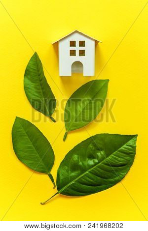 Miniature Toy Model House With Green Leaves On Yellow Colourful Trendy Backgdrop. Eco Village, Abstr