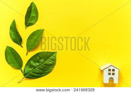 Miniature Toy Model House With Green Leaves On Yellow Colourful Trendy Backgdrop. Eco Village, Abstr