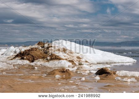 Raven Sitting On A Sandy And Snowy Hill Against The Background Of Foggy Mountains And Rivers