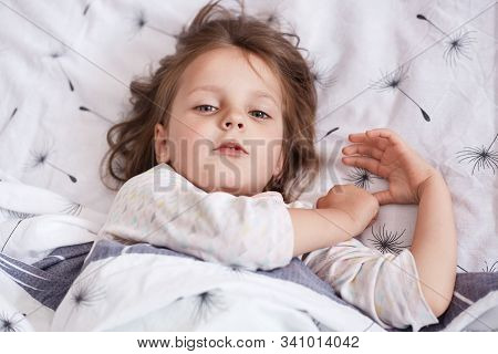 Top View Of Little Sleepy Child Looking Directly At Camera, Waking Up Early, Lying In Bed, Having Fa