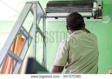 Workers Repairs And Cleans The Air Conditioner In The Room. Steel Ladder Used By The Worker To Climb