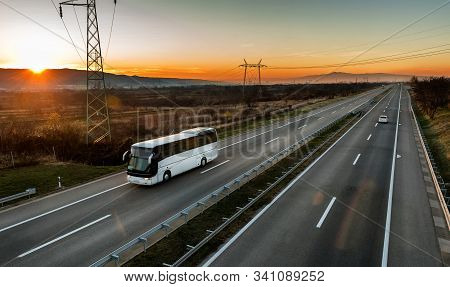 White Bus Traveling On A Country Highway Under Amazing Orange Sunset Sky. Highway Transportation Of 