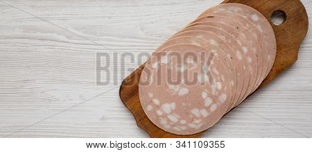Sliced Mortadella Bologna Meat On A Rustic Wooden Board Over White Wooden Surface, View From Above. 
