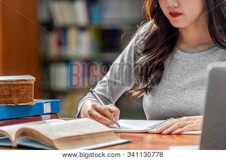 Closeup Asian Young Student Hand Writing Homework And Using Technology Laptop In Library Of Universi