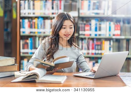 Asian Young Student In Casual Suit Doing Homework And Using Technology Laptop In Library Of Universi