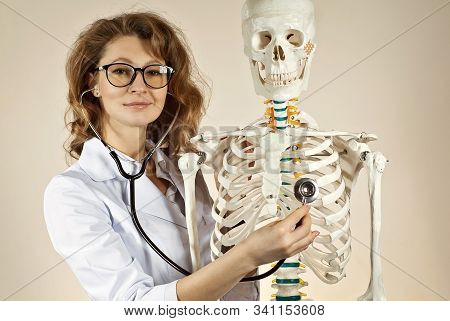 Woman In White Medical Gown. Doctor With Skeleton Layout On Yellow Background. The Doctor In The Gla