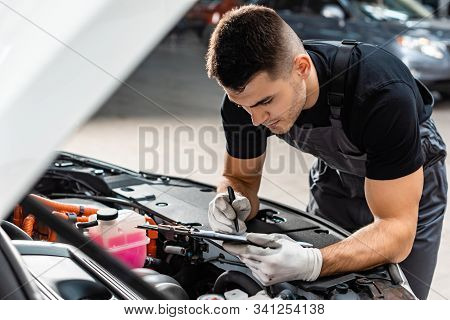 Selective Focus Of Mechanic Writing On Clipboard While Inspecting Car Engine Compartment