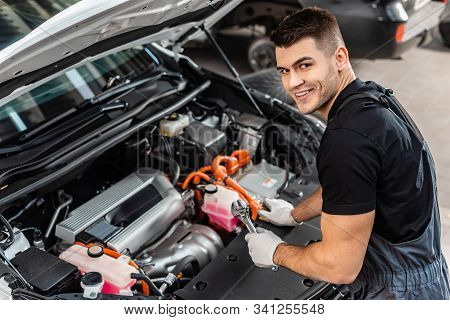 Handsome Mechanic Inspecting Car Engine Compartment And Smiling At Camera