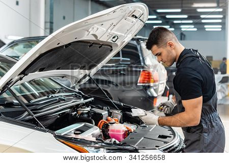 Young Mechanic Wiping Oil Dipstick With Rag Near Car Engine Compartment