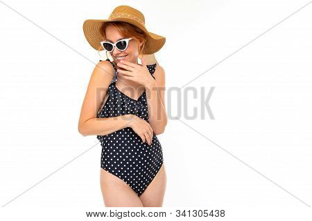 Beautiful Girl In A Retro Bathing Suit And A Straw Summer Hat And Sunglasses Laughs On A White Backg