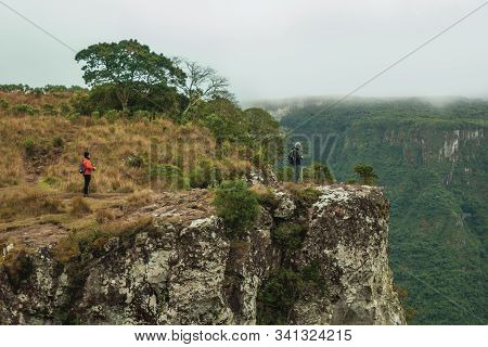 Cambara Do Sul, Brazil, July 17, 2019. People On Steep Rocky Cliff In Fortaleza Canyon With Fog Comi