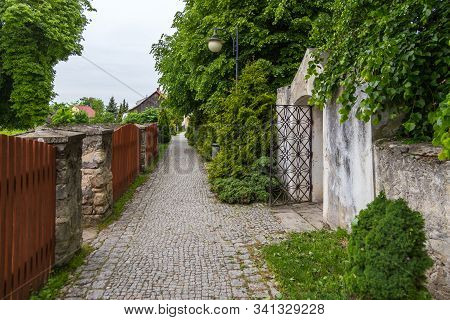 Szydlow, Poland- 23 May 2015: Narrow Cobbled Street, Along Old Walls With Entances. Garden Behind Th