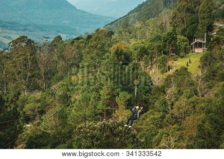 Canela, Brazil - July 21, 2019. Man Descending By Cables In A Sport Called Zip-line Over Green Fores