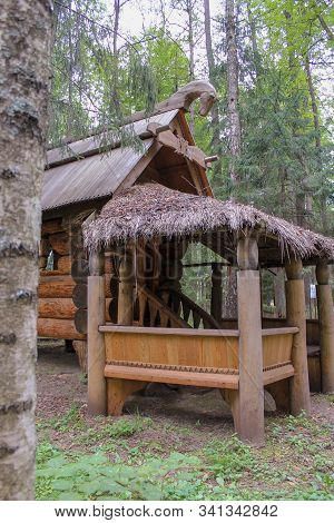 View From Behind A Tree Trunk On A Decorative Hut On Pillars Of Solid Logs With A Thatched Roof In T
