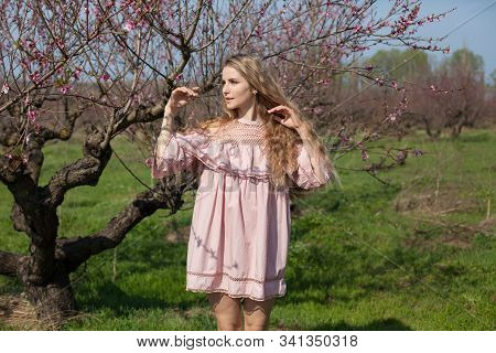 Beautiful Blonde Woman In Pink Dress Walks Through The Flowering Garden Spring