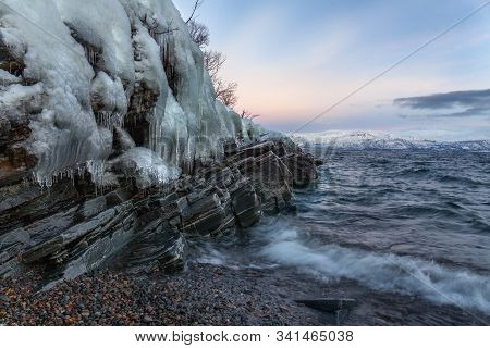 Icicles Hanging From The Rocks On The Shore Tornetrask, Sweden. Beautiful Waves. Long Shutter Speed