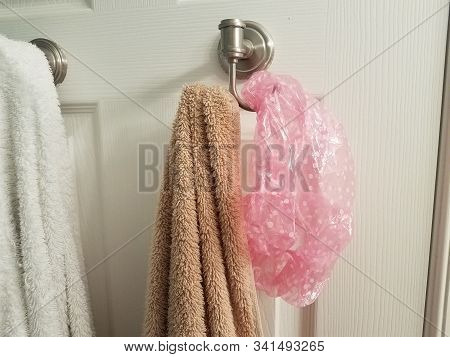 White And Brown Towel On Hook On Bathroom Door With Pink Showercap
