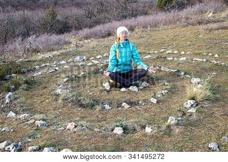 An Adult Mature Woman Practices Yoga In The Center Of A Spiral Laid Out Of Stones On The Top Of Para