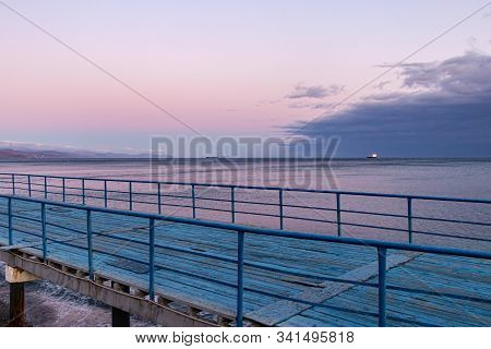 Amazing Colors On The Sea At Sunset - A Pink Sky Is Reflected In The Water And A Cyan Wooden Jetty F