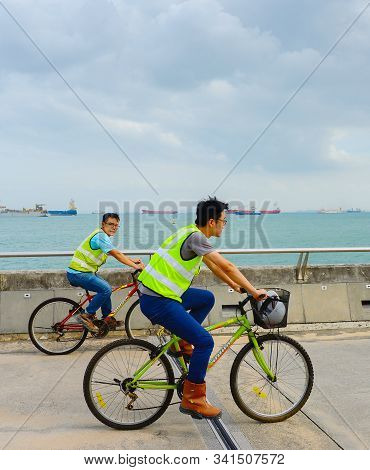 Singapore - February 16, 2107: Two Worker In Uniform Riding The Bicycles At Singapore Harbor. Indust