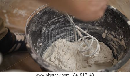 Builder Mixing Plaster In A Bucket Using An Electric Mixer. Builder Mixes The Mixture In A Bucket Us