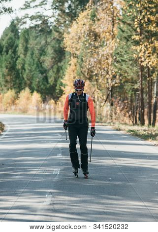 Training An Athlete On The Roller Skaters. Biathlon Ride On The Roller Skis With Ski Poles, In The H