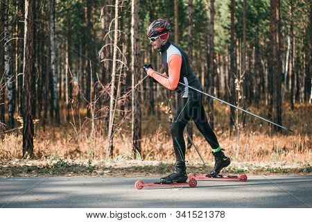Training An Athlete On The Roller Skaters. Biathlon Ride On The Roller Skis With Ski Poles, In The H