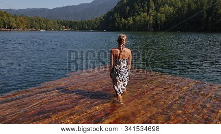 Woman Walk On Water On Pier In Sunglasses And A Boho Silk Shawl. Girl Rest On Flood Wood Underwater 