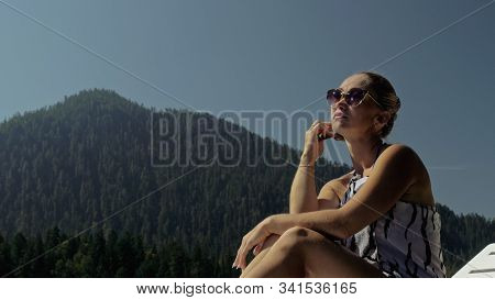 Woman Lie On A Sunbed In Sunglasses And A Boho Silk Shawl. Girl Rest On A Flood Wood Underwater Pier