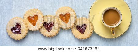 a row of jam heart biscuits with a cup of coffee on textured paper, coffee break, dessert, love or Valentines Day concept