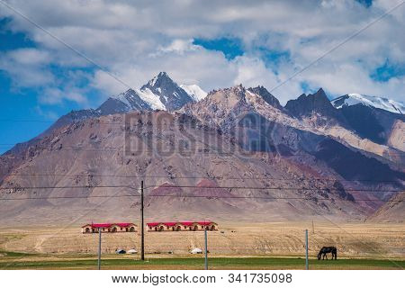Majestic Snow-capped Mountains Peak With Cloudy Blue Sky In Pamirs Plateau,alone Black Horse Grazing