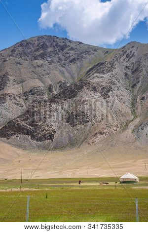 White Mongolian Traditional Yurt And A Woman On Pastures At The Foot Of Rocky Mountain In Pamirs Pla