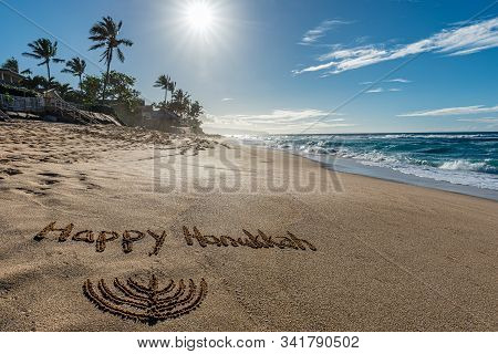 Happy Hanukkah Written In The Sand With A Hanukkiah With A Tropical Beach And Ocean In The Backgroun