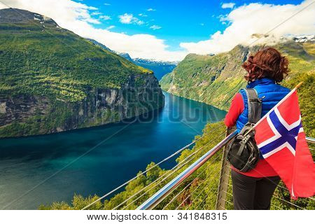 Female Tourist With Norwegian Flag Enjoying Scenic View Over Fjord Geirangerfjord.