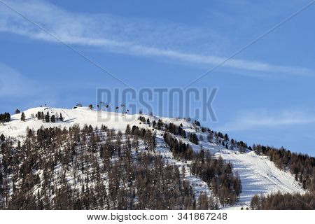 Top Of Snowy Ski Slope With Ski-lifts, Traces And Forest In High Winter Mountains At Sunny Morning. 