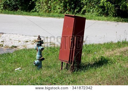 Leaning Dark Red Metal Fire Department Box Locked With Padlock Next To Dilapidated Rusted Light Blue