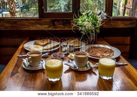 Two Breakfasts Consisting Of Coffee With Milk, Orange Juice, Butter, Jams, Toast, Eggs And Omelets, 