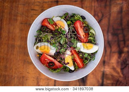 Healthy vegetable salad with mixed green leaves (arugula, mesclun, lettuce), eggs, black olives, tomato and bean sprouts. Wooden background. Top view