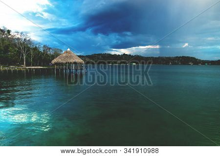 Wooden Old Dock During Sunset With Reflexions And Massive Raincloud At Lake Itza, El Remate, Peten, 