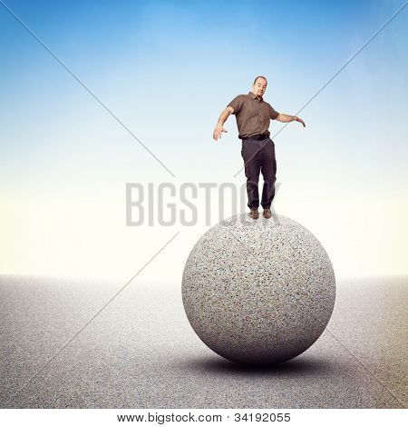 homem tenta equilibrar-se isolado na esfera de pedra grande