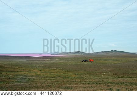 Autotourism. A Lonely Car With A Residential Trailer In The Steppe With A Pink Lake On The Horizon. 