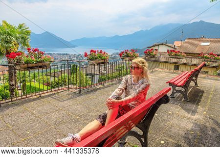 Woman Sitting On Top Of Lake Maggiore In Switzerland. Swiss Bench At Aerial View Lookout From Orseli