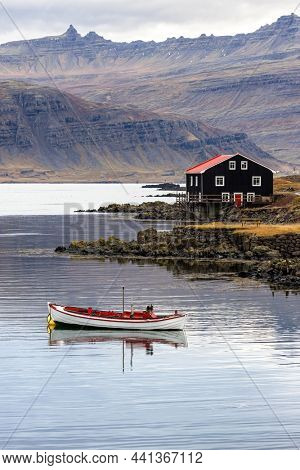 Small boat and black wooden house, Djupivogur, Eastfjords, Iceland. Vertical shot in autumn with mountain background. 