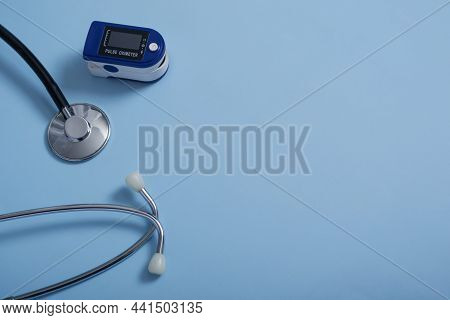 Flat Composition With Pulse Oximeter And Stethoscope On Blue Background.a Pulse Oximeter Used To Mea